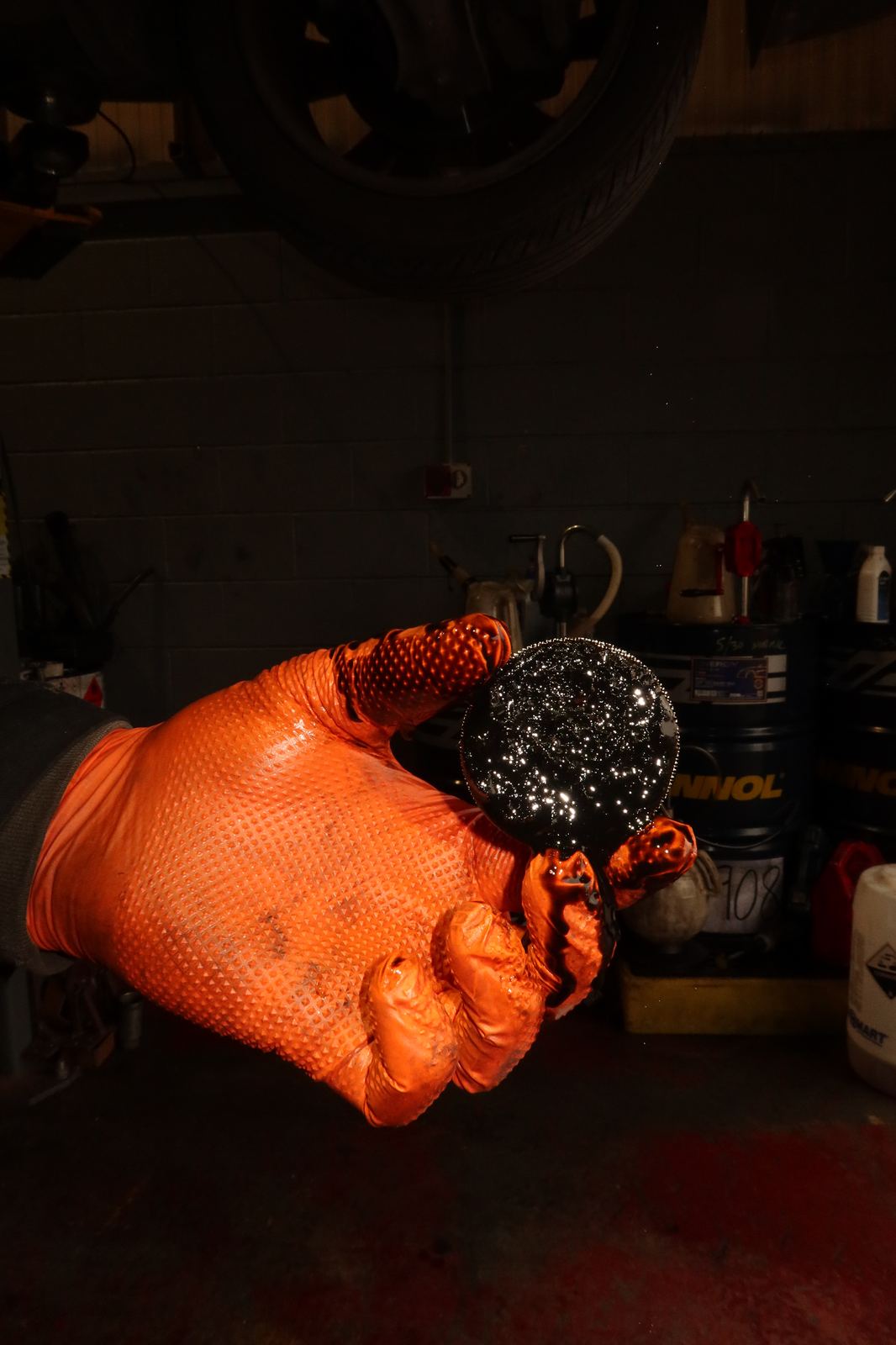 Technician holding up an oil pickup strainer caked in wet belt sludge in the workshop